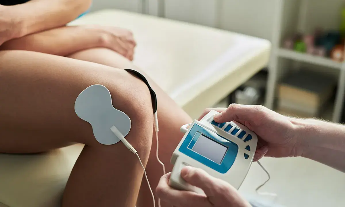 Elektrostymulacja TENS na kolanie. Terapeuta reguluje urządzenie, minimalizując potencjalne prądy TENS skutki uboczne.
