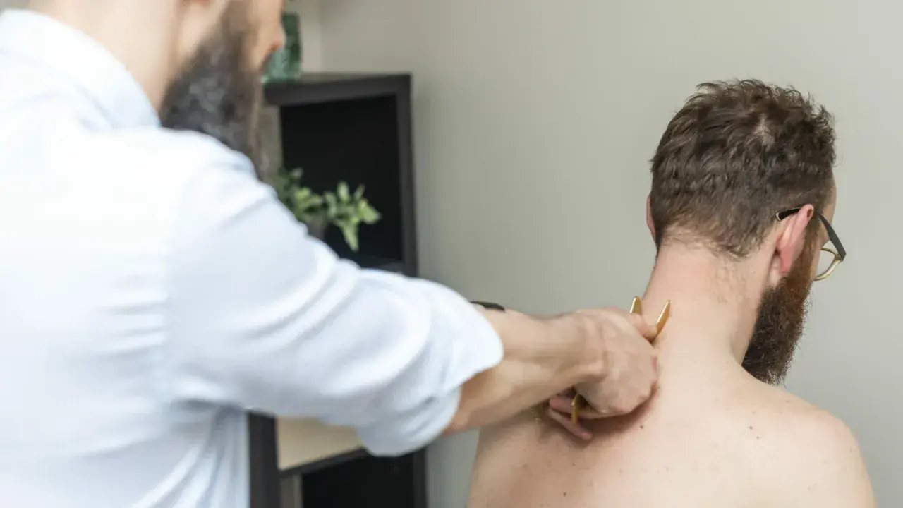 Fizjoterapeuta wykonuje masaż karku pacjentowi. Czasem po rehabilitacji odczuwamy większy ból, ale to część procesu powrotu do zdrowia.