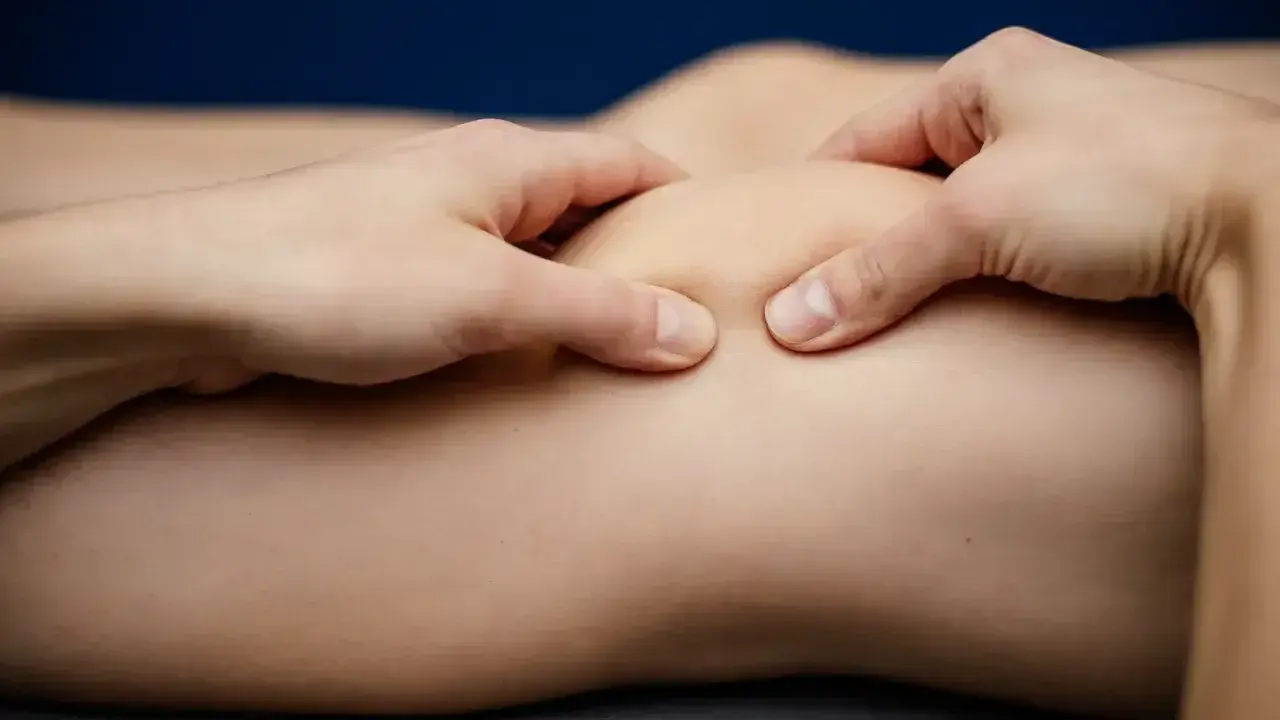 Fizjoterapeuta wykonuje masaż stawu kolanowego, pomagając w leczeniu chondromalacji rzepki. Ćwiczenia wzmacniające są kluczowe.