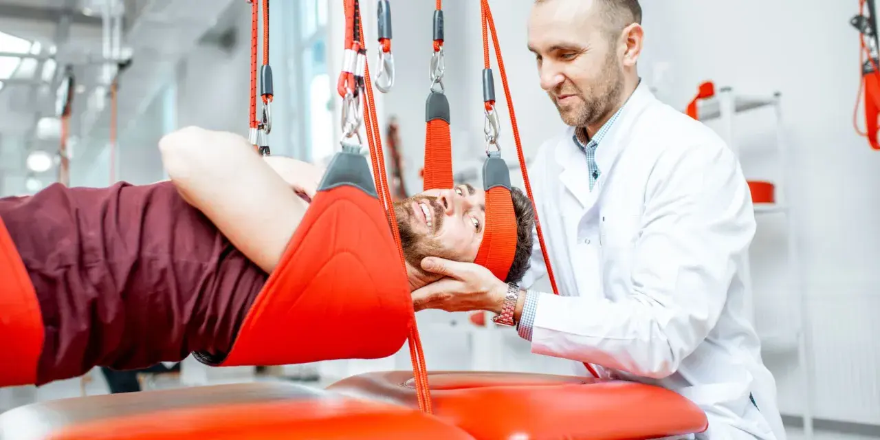 Fizjoterapeuta pomaga pacjentowi w ćwiczeniach odciążających kręgosłup lędźwiowy, stosując system podwieszeń.