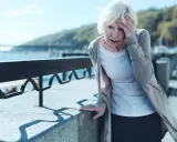 Starsza kobieta z bólem głowy opiera się o balustradę, czując zawroty głowy. Może to być problem z układem przedsionkowym.