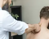 Fizjoterapeuta wykonuje masaż karku pacjentowi. Czasem po rehabilitacji odczuwamy większy ból, ale to część procesu powrotu do zdrowia.