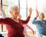 Uśmiechnięte seniorki wykonują ćwiczenia przeciwzakrzepowe, unosząc ręce w górę.