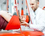 Fizjoterapeuta pomaga pacjentowi w ćwiczeniach odciążających kręgosłup lędźwiowy, stosując system podwieszeń.