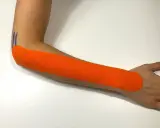Pomarańczowy plaster kinezjotaping na przedramieniu, wspierający leczenie łokcia tenisisty. Fizjoterapia w działaniu.