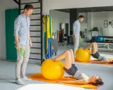 Fizjoterapeuta nadzoruje ćwiczenia z piłką, które pomagają jak wzmocnić mięsień czworogłowy.