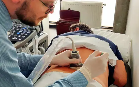 Lekarz wykonuje badanie USG kręgosłupa, skupiając się na ocenie stawów międzykręgowych pacjenta.