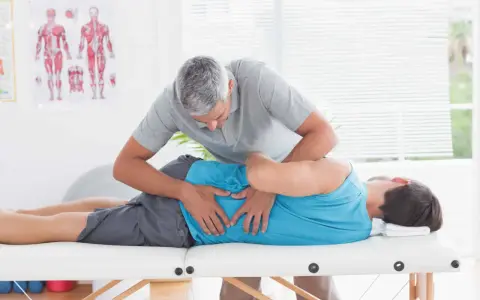 Fizjoterapeuta wykonuje zabieg metodą McKenziego na pacjencie leżącym na kozetce.
