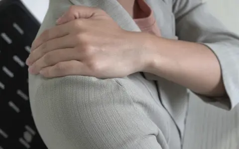 Dłoń na ramieniu, odczuwając ból, który może być objawem Lhermitte'a.