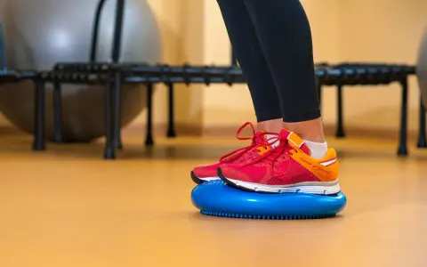 Nogi w butach sportowych stoją na niebieskiej poduszce sensorycznej, wykonując ćwiczenia równowagi.