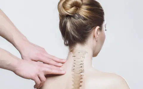 Dłonie terapeuty badają kręgosłup szyjny kobiety. Czy to objawy whiplash?