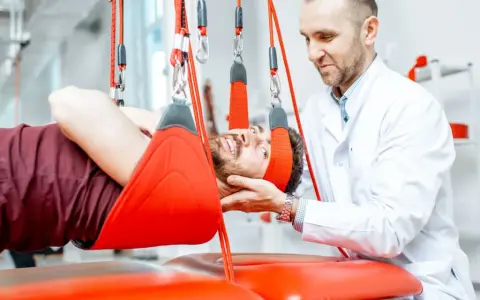 Fizjoterapeuta pomaga pacjentowi w ćwiczeniach odciążających kręgosłup lędźwiowy, stosując system podwieszeń.