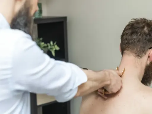 Fizjoterapeuta wykonuje masaż karku pacjentowi. Czasem po rehabilitacji odczuwamy większy ból, ale to część procesu powrotu do zdrowia.