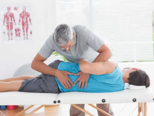 Fizjoterapeuta wykonuje zabieg metodą McKenziego na pacjencie leżącym na kozetce.