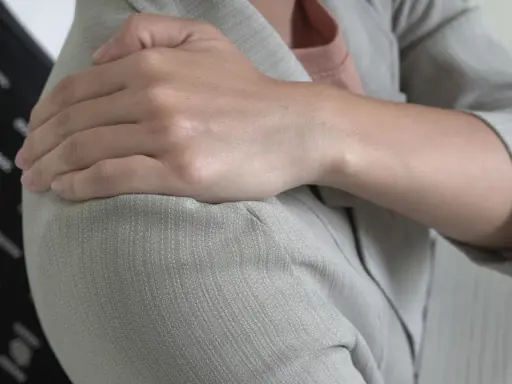 Dłoń na ramieniu, odczuwając ból, który może być objawem Lhermitte'a.