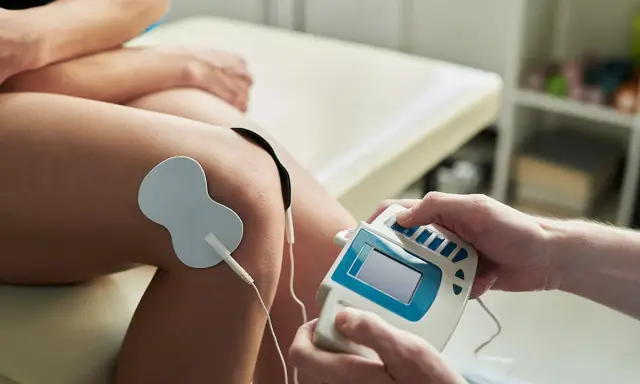 Elektrostymulacja TENS na kolanie. Terapeuta reguluje urządzenie, minimalizując potencjalne prądy TENS skutki uboczne.