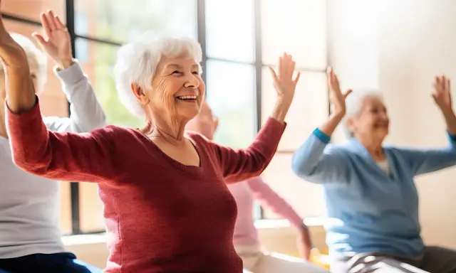 Uśmiechnięte seniorki wykonują ćwiczenia przeciwzakrzepowe, unosząc ręce w górę.