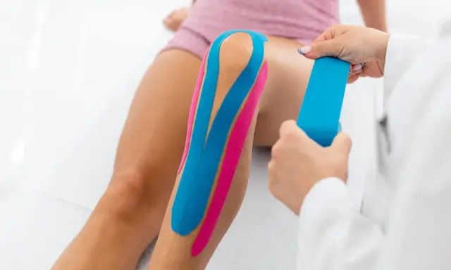 Fizjoterapeuta aplikuje plastry taping na kolano pacjentki, poprawiając stabilizację i wsparcie.