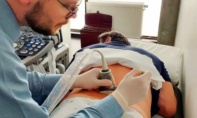 Lekarz wykonuje badanie USG kręgosłupa, skupiając się na ocenie stawów międzykręgowych pacjenta.