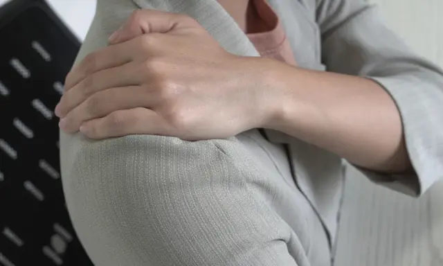 Dłoń na ramieniu, odczuwając ból, który może być objawem Lhermitte'a.