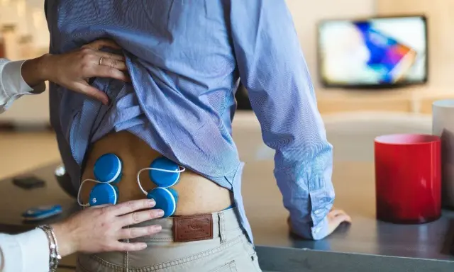 Elektrostymulacja jak często? Terapeuta umieszcza elektrody na plecach pacjenta, przygotowując go do zabiegu.