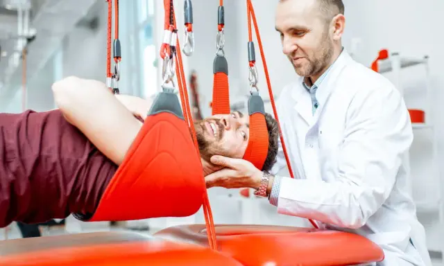 Fizjoterapeuta pomaga pacjentowi w ćwiczeniach odciążających kręgosłup lędźwiowy, stosując system podwieszeń.