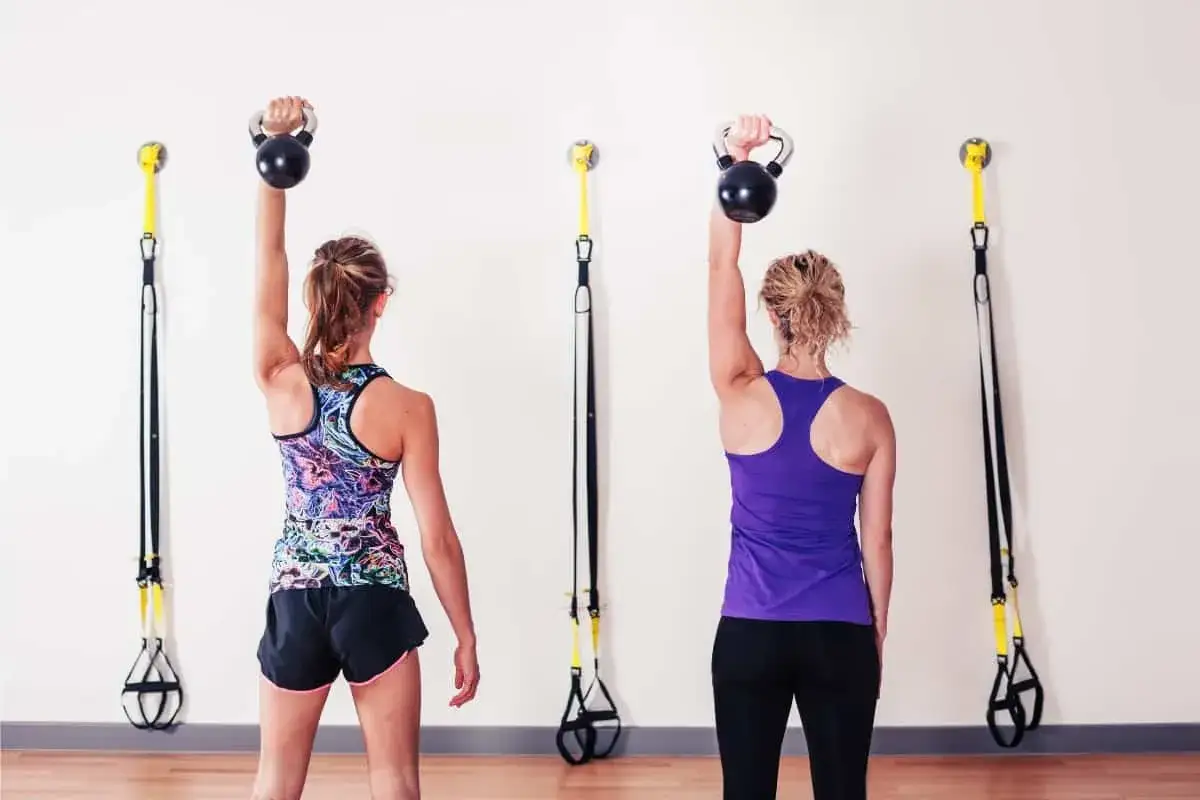 Dwie kobiety ćwiczą z kettlebellami, wspierając rehabilitację po uszkodzeniu stożka rotator&oacute;w.