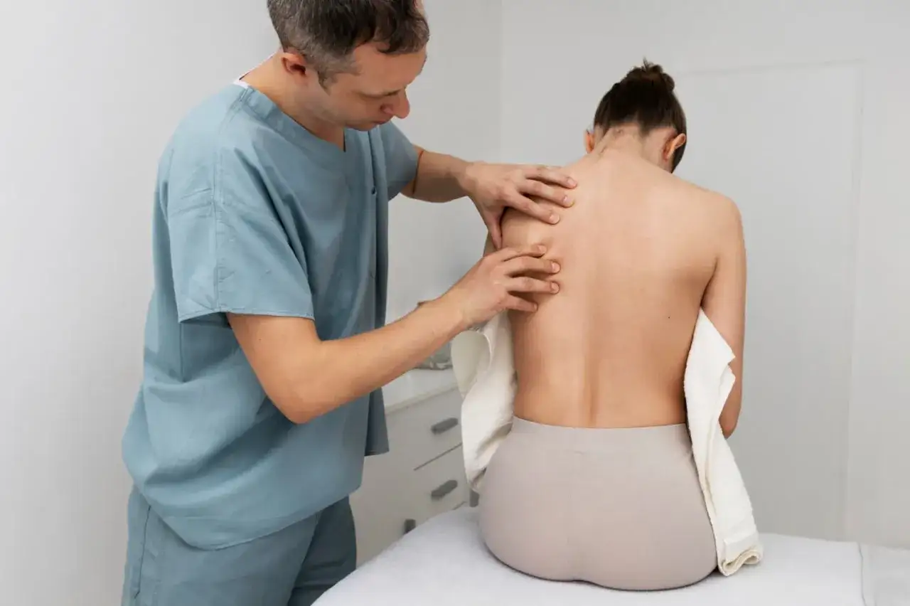 Fizjoterapeuta bada plecy pacjentki po operacji kręgozmyku, oceniając ewentualne powikłania.