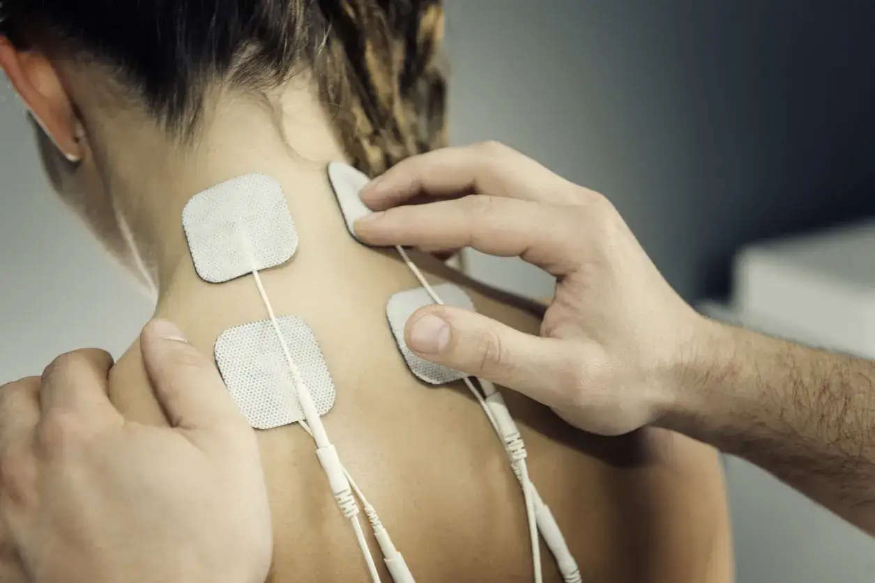 Elektrostymulacja jak często? Terapeuta umieszcza elektrody na karku pacjentki, przygotowując ją do zabiegu.