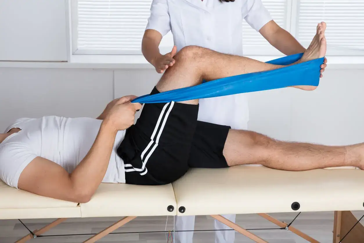 Fizjoterapeuta pomaga pacjentowi w ćwiczeniach na chondromalację rzepki, używając taśmy oporowej do wzmocnienia mięśni.