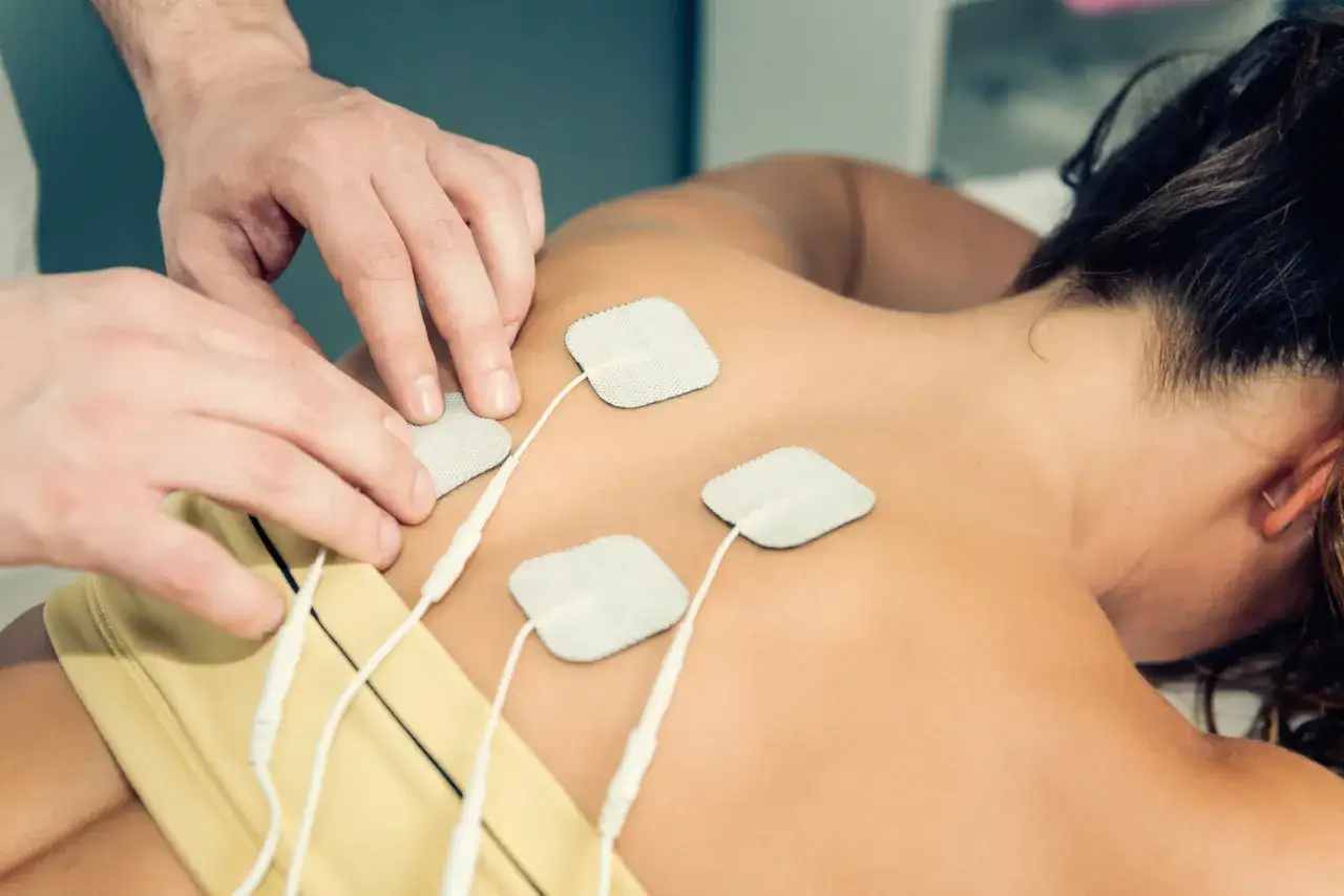 Fizjoterapeuta umieszcza elektrody na plecach pacjentki. Prądy TENS mogą przynieść ulgę, ale warto znać potencjalne skutki uboczne.